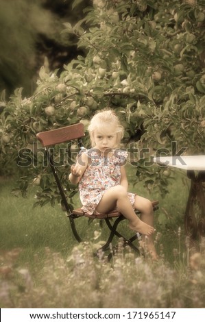 Cute little girl sitting in a garden chair in a lush garden, retro style, an enchanting atmosphere lies over the scene. Retro style picture