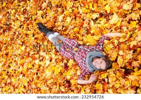 Attractive woman lying in a bed of colorful yellow and orange autumn leaves scattered on the ground, marking the change of the seasons