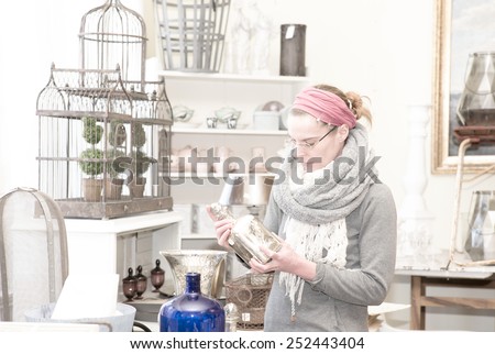 Attractive woman visiting an antique shop and looking for precious nice things. Desaturated colors, high-key effect.
