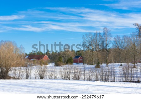 Old red wooden barns of a farm in Sweden under a clear blue sky in winter.