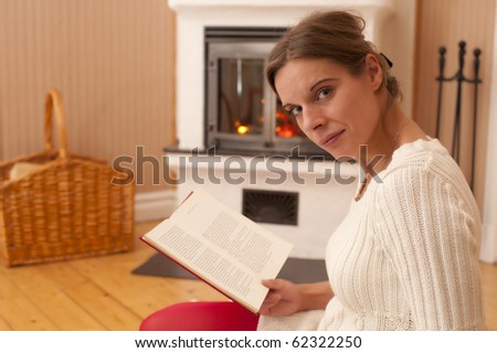 Young woman sitting in front of a fireplace, reading a book. Warm colors, looks like at home during a winter day.