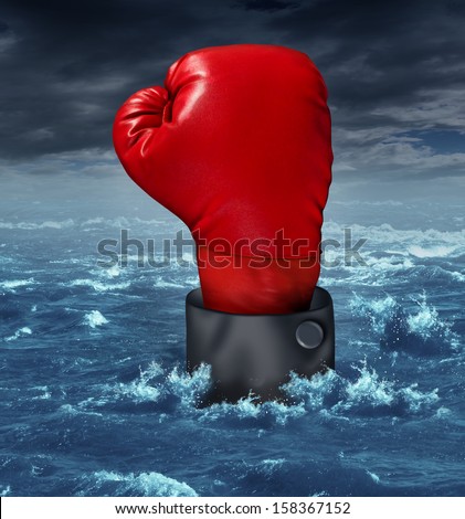 Drowning the competition business concept with the hand of a businessman wearing a red boxing glove reaching up struggling to survive in turbulent ocean water as a metaphor for financial crisis.