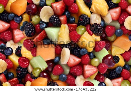 Fruit salad background as fresh berries and cut fruits as blueberry blackberry strawberries melon cantaloupe raspberry pineapple banana and grapes as a symbol of healthy lifestyle and living well.