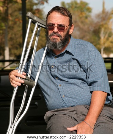 Older gentleman resting on a park bench while holding his crutches and contemplating his accident
