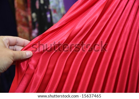 Woman shopping for clothing and inspecting a red pleated skirt or dress