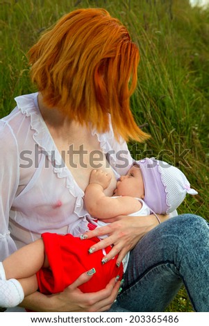 Mother breastfeeding her baby on a great sunny day in a meadow with lots of green grass