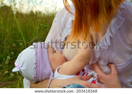 Mother breastfeeding her baby on a great sunny day in a meadow with lots of green grass