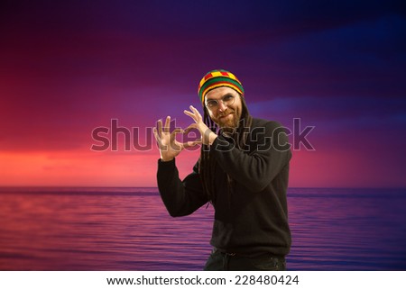 man with dreadlocks holds hands in a heart shape. sunset at sea. variety of colors and hues of the rising sun