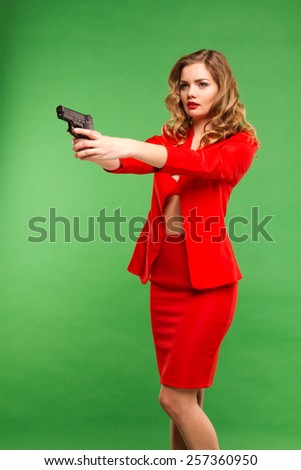 passionate young woman in red dress standing on a green background with a gun. lifestyle