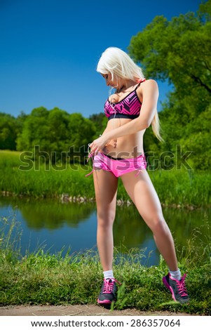 Sexy sport in nature. Blonde girl in the woods near the water does sports exercises in short shorts and a tank top