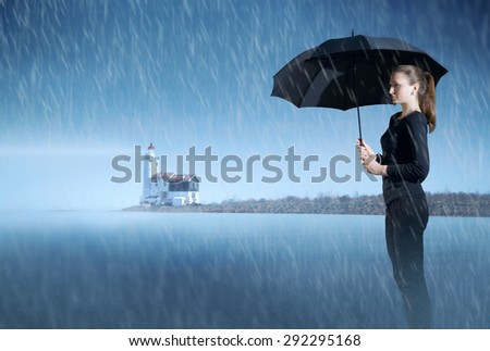 girl with an umbrella standing in the mist on the ocean at night in the rain, on the background of the lighthouse. rainy weather