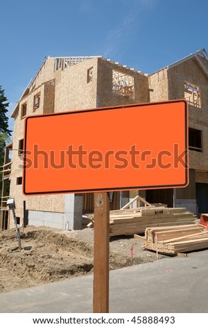 A blank orange construction sign against wood frame building construction