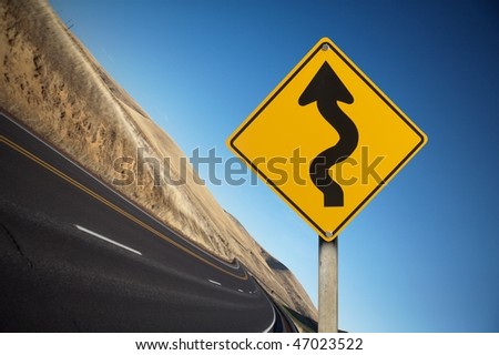Winding yellow traffic sign against winding road