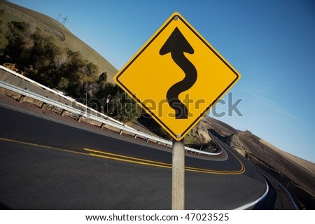 Winding yellow traffic sign against winding road