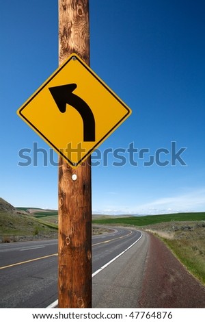 Warning turn left traffic sign on electric wooden pole winding road on background