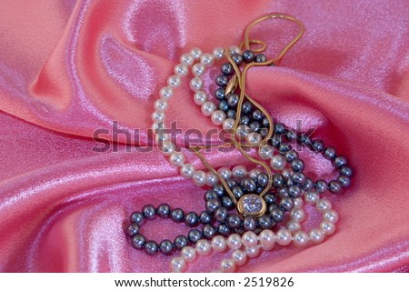 White and black pearl necklaces with diamond necklace on pink cloth background.