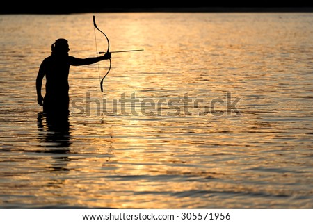 Silhouette archery shoots a bow at a target in sunset sky and cloud