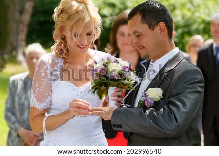 beautiful young couple in wedding ceremony outdoor, blonde bride with flower and groom exchange of wedding rings