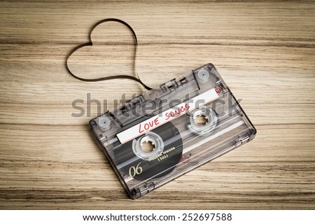 Audio cassette tape on wooden backgound. Film shaping heart, Valentine postcard. Label text love songs.