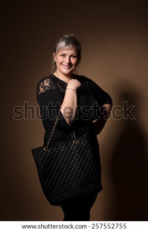 portrait of beautiful smiling plus size young blond woman posing with designer handbags and black dress