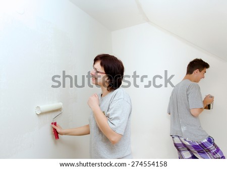 housewife with son painting wall in child room to white at home