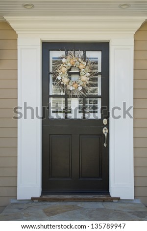 Front door of an upscale home/Vertical shot of a black front door on an upscale home with a wreath and windows with reflection.