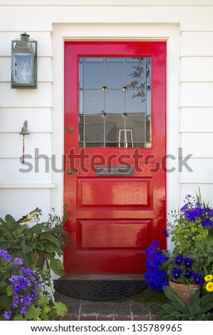 Red front door of an upscale home/Vertical shot of a red front door on a home with a mail slot, plants, doorbell, brick flooring and reflection in the window.