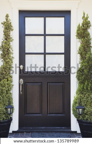 Front Door Of An Upscale Home/Vertical Shot Of A Black Front Door Of An Upscale Home With White Windows, Plants, Porch Lights And Stone Flooring