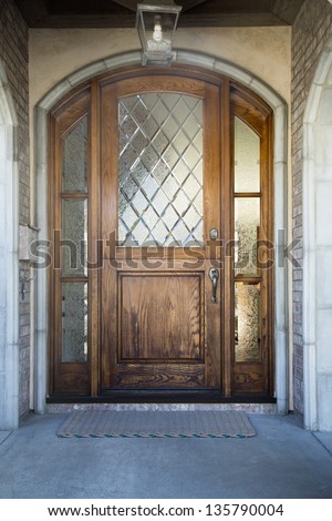 Front door of an upscale home/Vertical shot of a wooden front door on an upscale home with large frosted glowing windows and view of mailbox, door mat and light fixture
