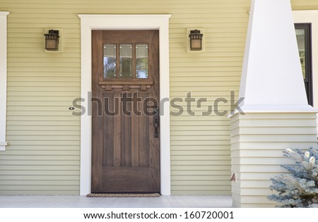 Closed Wooden Door Of A Home With Yellow Siding In Daytime.