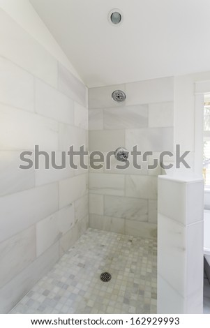 An Modern, Marble-Tiled, Open-Aired Walk-In Shower With Shower Head, Fixture, And Drain.