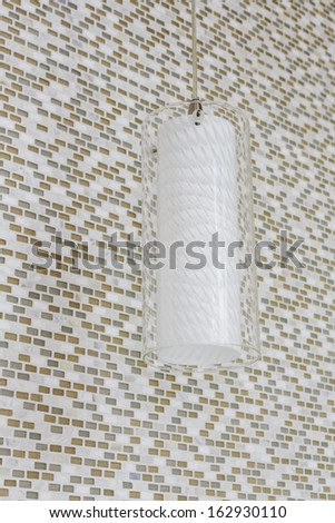 An unlit light fixture hanging from the ceiling of a home bathroom against a mosaic tile wall.