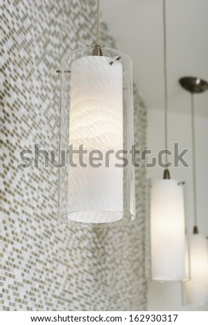 An arrangement of lit light fixtures hanging from the ceiling against a mosaic tile wall in a bathroom.