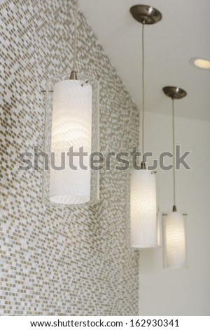 An Arrangement Of Lit Light Fixtures Hanging From The Ceiling Against A Mosaic Tile Wall.