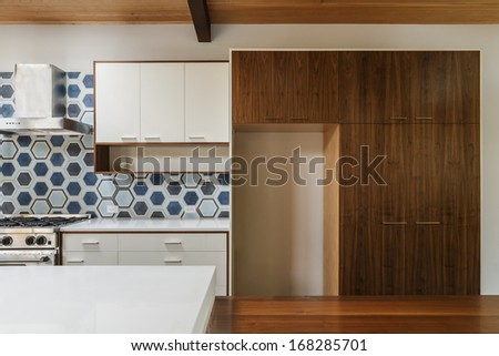 A kitchen with wooden cabinet, wooden dining table, white cupboards and countertop, hexagonal tile, and gas stove.