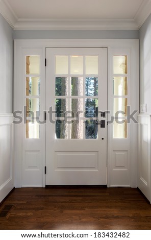 Vertical shot of an closed, wooden front door from the interior of an upscale home with windows.