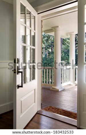 Vertical wide  shot of an open, wooden front door from the interior of an upscale home with windows.