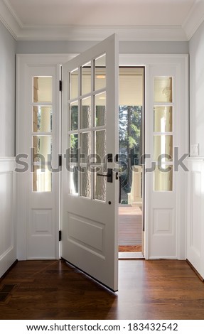 Vertical shot of an open, wooden front door from the interior of an upscale home with windows.