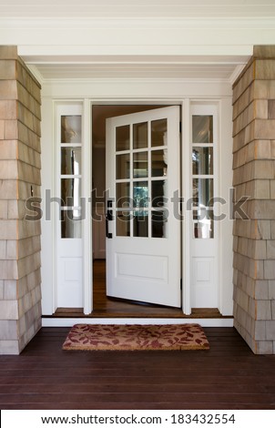 Vertical shot of an open, wooden front door from the exterior of an upscale home with windows.
