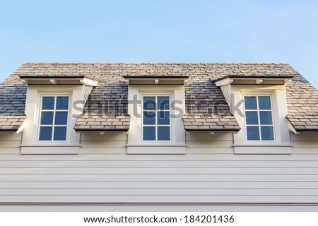 An upwards view at 3 attic windows of a white family home. The house is white siding with white trim. Roof detail can be seen, as well as a clear, blue sky.