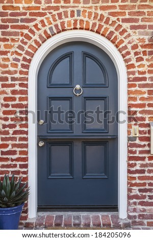 Glossy blue door to classic brownstone home. A lacquered blue front door to a classic brownstone family home. Door is featured under brick arch, with door knocker, and a plant in blue pot.