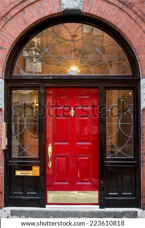 Closeup of Red Door In Black Archway Door Frame with Windows on Brick Building