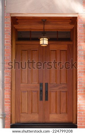 Modern Natural Wood Double Doors with Overhead Hanging Lamp in Brick Building