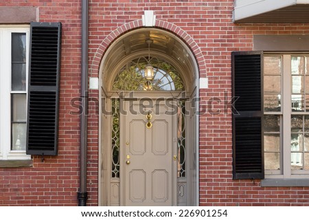Tan Front Door with Lunette Window and Arch in Brick Building with Black Shutters and Windows in Frame