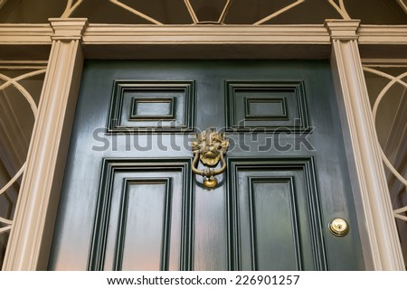 Close Up of Gold Door Knocker on Green Paneled Front Door with Molded Door Frame and Ornate Windows