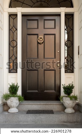 Close Up of Black Front Door with Lunette and Side Windows in White Door Frame with Potted Plants and Doormat