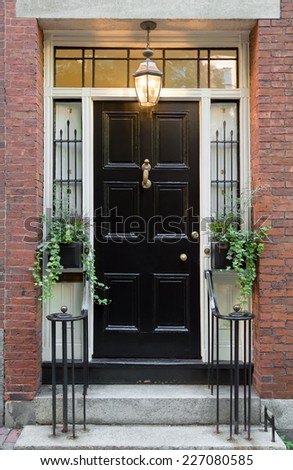 Black Front Door with Surrounding Windows and White Door Frame in Brick Building with Standing Potting Plants