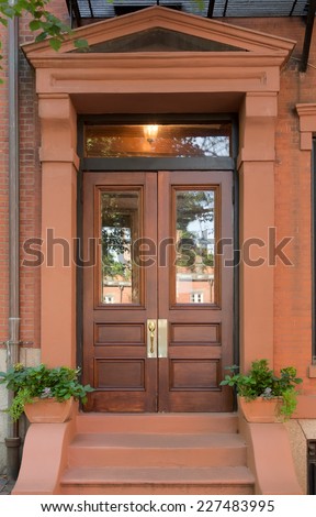 Double Natural Wood Front Doors with Windows in Brownstone Portico with Small Potted Plants and Steps