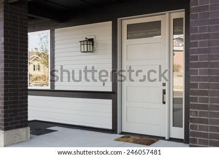 Horizontal Angled Shot of White And Black Front Entryway with White Siding, a White Front Door, and Black Framing
