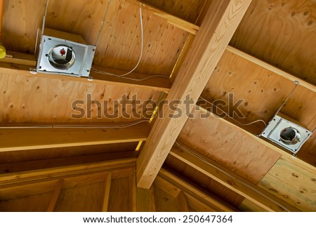 The interior view of the construction of a pitched roof showing the ridge, rafters and sheathing as well as early stages of electrical wiring for interior lighting. Horizontal shot.